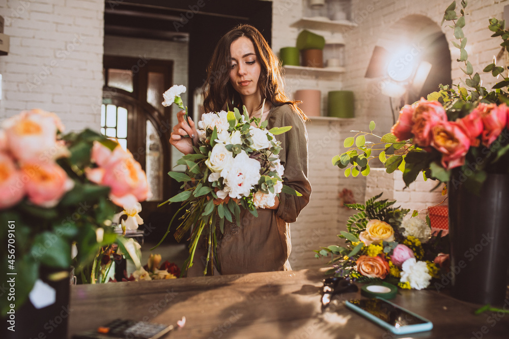 Fototapeta premium Woman florist at her own floral shop taking care of flowers