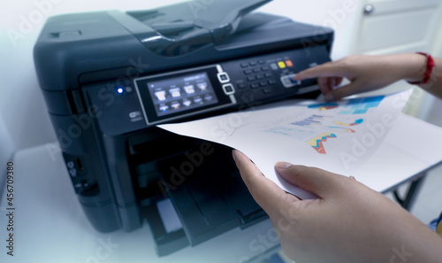 Office worker prints paper on multifunction laser printer. Copy, print, scan, and fax machine in office. Document and paper work. Print technology. Hand press on photocopy machine and holding paper.
