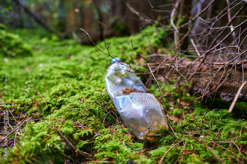 Fototapeta Naklejka Na Ścianę i Meble -  A carelessly throw away plastic water bottle nestled in the moss on a forest path. Plastic trash in the forest. Tucked nature. Season of autumn. World ecology problem.