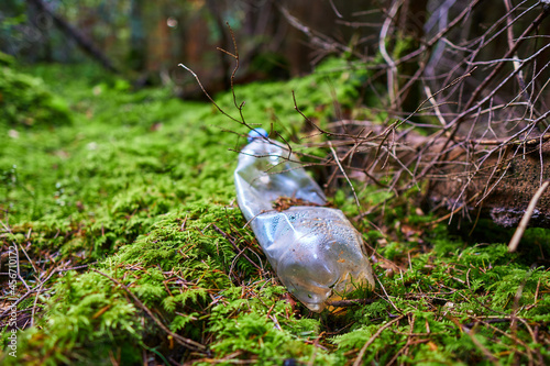 A carelessly throw away plastic water bottle nestled in the moss on a forest path. Plastic trash in the forest. Tucked nature. Season of autumn. World ecology problem.