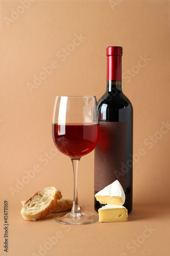 Bottle and glass of wine, cheese and bread on beige background