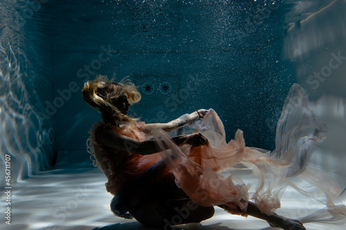 A girl with long dark hair swims underwater in a pink dress and with a crown on her head, like an underwater queen. Fairy tale suitable for advertising 