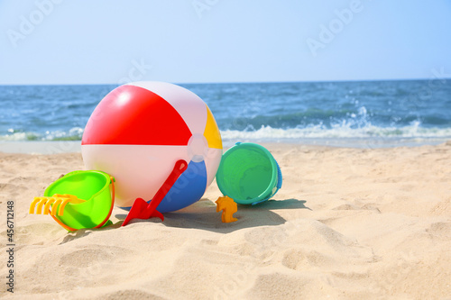 Different sand toys and beach ball near sea, space for text