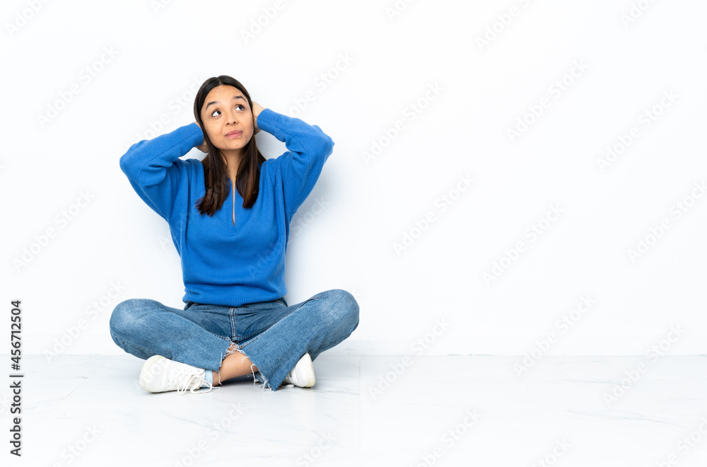 Young mixed race woman sitting on the floor isolated on white background frustrated and covering ears Young mixed race woman sitting on the floor isolated on white background frustrated and covering ears