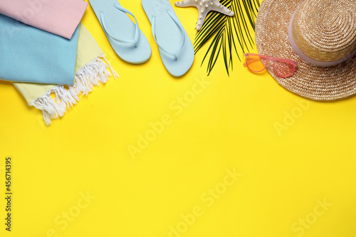 Beach towel, flip flops, straw hat and sunglasses on yellow background, flat lay. Space for text