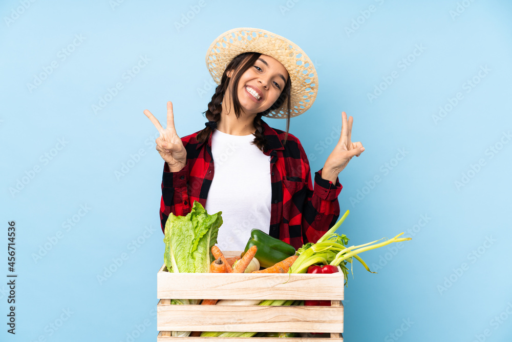 Young farmer Woman holding fresh vegetables in a wooden basket showing victory sign with both hands