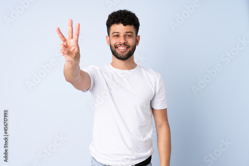 Young Moroccan man isolated on blue background happy and counting three with fingers © luismolinero