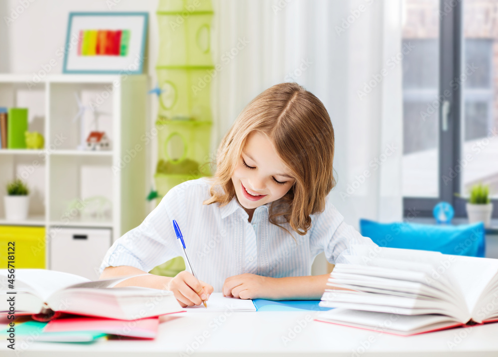 education, elementary school, learning and people concept - happy smiling girl with notebook and pen sitting at table over home background education, elementary school, learning and people concept - happy smiling girl with notebook and pen sitting at table over home background