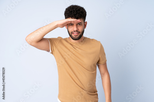 Young Moroccan man isolated on blue background looking far away with hand to look something