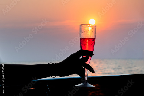 Hand of woman with drink in swimsuit at sunset at yacht