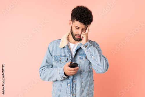 Young Moroccan man using mobile phone isolated on pink background with headache © luismolinero