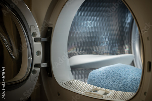 View of the tumble dryer or washing machine with the door open and a blue towel inside