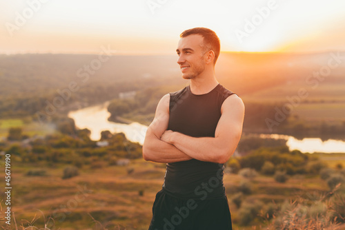 Portrait of a young man with crossed arms at sunset with a beautiful landscape as a background.
