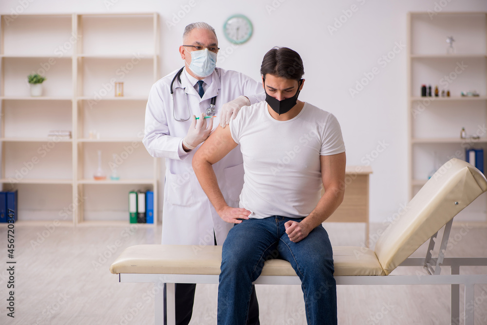 Fototapeta premium Young male patient visiting old doctor in vaccination concept
