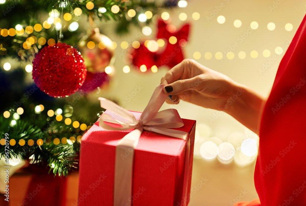winter holidays, celebration and people concept - close up of woman with gift box at christmas tree at home winter holidays, celebration and people concept - close up of woman with gift box at christmas tree at home