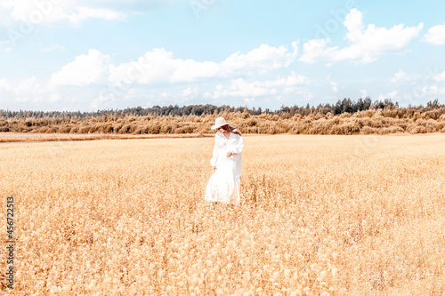 young woman plus size model in long white drees on field of ripe cereals and a blue sky with clouds in autumn, a concept of harvest, agribusiness and farming