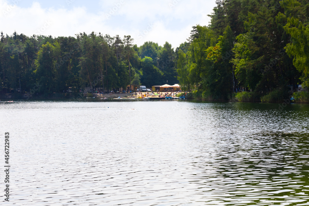 Jezioro Srebrne w Osowcu latem. Widok na jezioro, las i plażę z turystami Jezioro Srebrne w Osowcu latem. Widok na jezioro, las i plażę z turystami