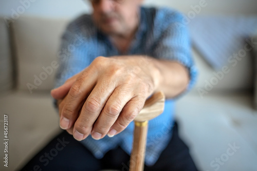 Portrait of happy senior man sitting at home with walking stick and smiling. Old man relaxing on sofa and looking at camera. Portrait of elderly man enjoying retirement. Health and medicine concept. © Jelena Stanojkovic