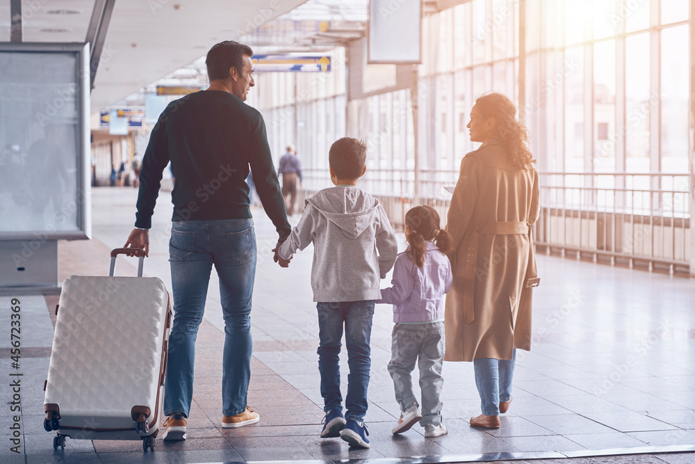 Fototapeta premium Full length rear view of family with two little kids walking by airport terminal