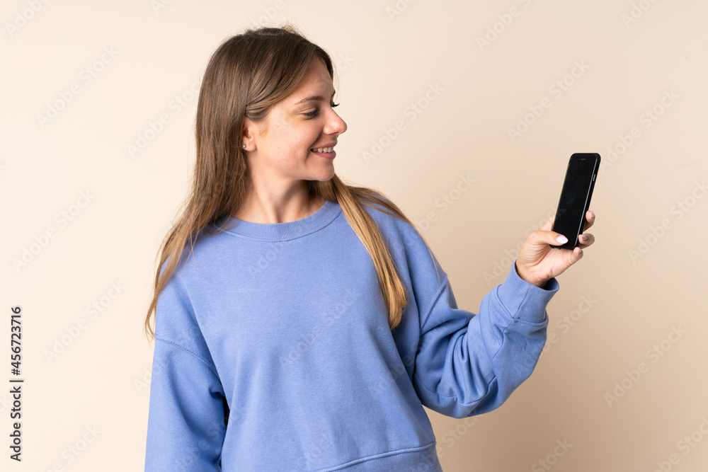 Young Lithuanian woman using mobile phone isolated on beige background with happy expression Young Lithuanian woman using mobile phone isolated on beige background with happy expression