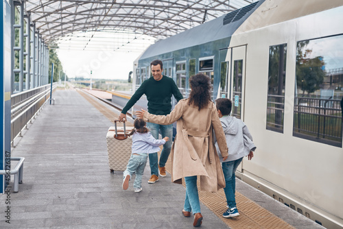 Full length of happy woman and two little kids meeting father on railroad station platform