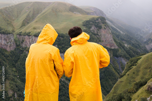 Two people in yellow raincoats admire the view of the mountains.