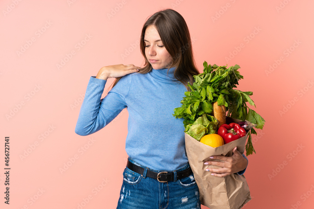 Young Lithuanian woman holding a grocery shopping bag suffering from pain in shoulder for having made an effort Young Lithuanian woman holding a grocery shopping bag suffering from pain in shoulder for having made an effort