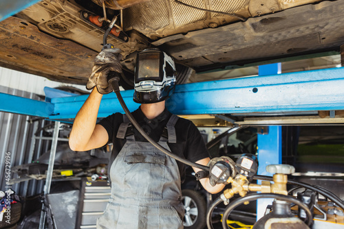 One young man, male auto mechanic, employee in dungarees making car service at garage, indoors. Concept of labor, occupation, business, caree, job