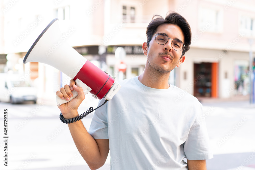 Young caucasian man at outdoors holding a megaphone and thinking Young caucasian man at outdoors holding a megaphone and thinking