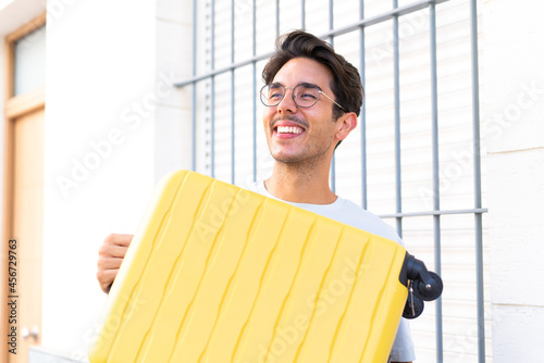 Young caucasian man at outdoors in vacation with travel suitcase