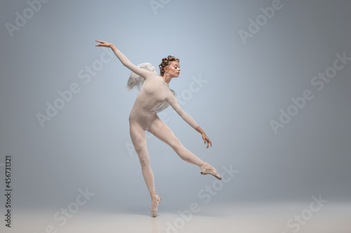 Fototapeta Naklejka Na Ścianę i Meble -  Young and graceful ballet dancer, ballerina dancing in image of angel with wings isolated on gray studio background. Art, motion, action, flexibility, inspiration concept.