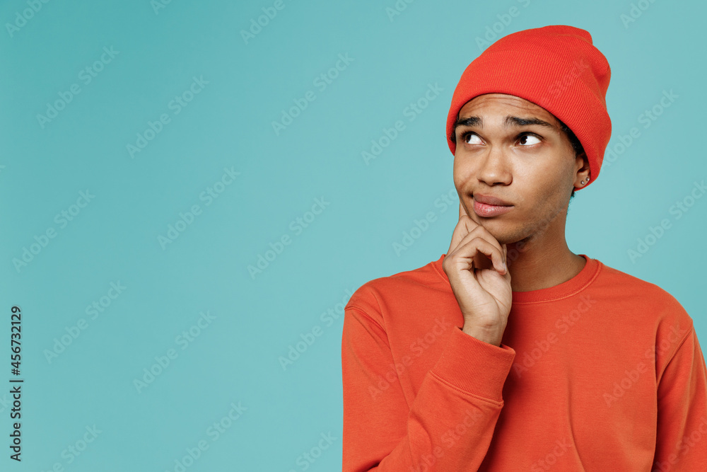 Young minded pensive thoughtful uncertain african american man 20s wear red shirt hat prop up chin look aside isolated on plain pastel light blue background studio portrait. People lifestyle concept Young minded pensive thoughtful uncertain african american man 20s wear red shirt hat prop up chin look aside isolated on plain pastel light blue background studio portrait. People lifestyle concept