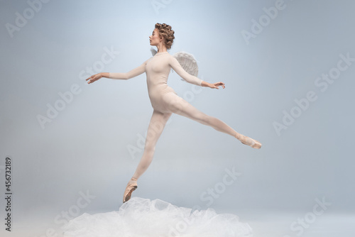 Young and graceful ballet dancer, ballerina dancing in image of angel with wings isolated on gray studio background. Art, motion, action, flexibility, inspiration concept.
