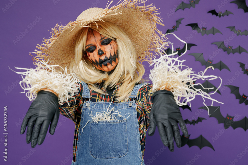 Fotka „Young woman with Halloween makeup mask in straw hat scarecrow  costume spread hand close eye pose as bugaboo isolated on plain dark purple  background studio portrait Celebration holiday party concept“ ze