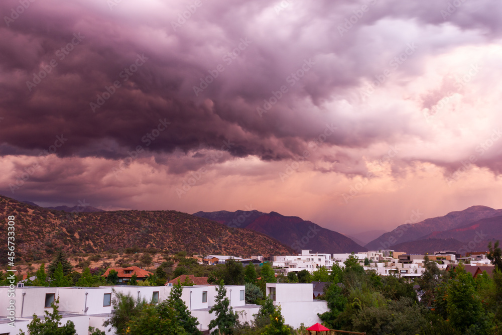 Colorful dramatic sky over residential area surrounded by mountains at sunset. Storm menace, beautiful nature concepts