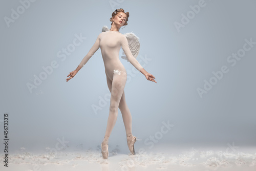 Full-length portrait of beautiful graceful ballerina dancing in image of angel with wings isolated on gray studio background. Art, motion, action, flexibility, inspiration concept. photo