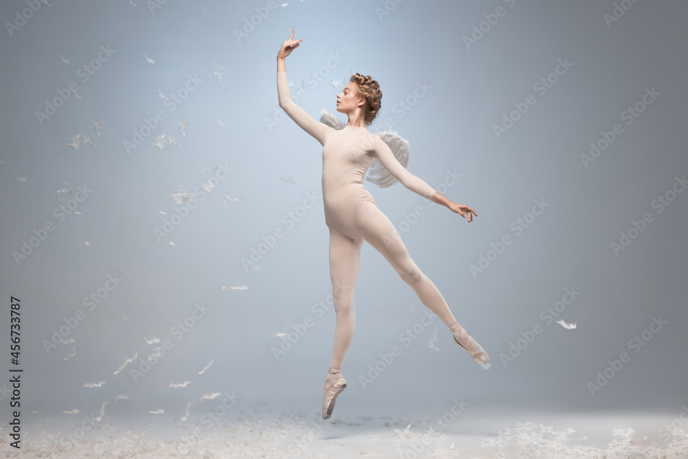 Fototapeta premium Full-length portrait of beautiful graceful ballerina dancing in image of angel with wings isolated on gray studio background. Art, motion, action, flexibility, inspiration concept.