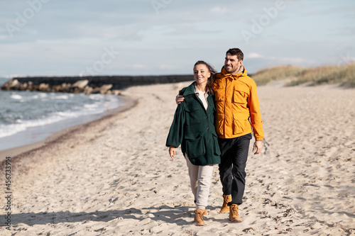 love, relationship and people concept - happy couple walking along autumn beach
