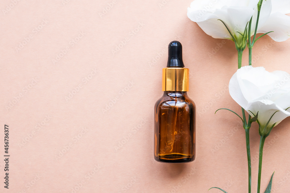 Cosmetic bottle with dropper and natural flower on a beige background. Top view, place for text. Cosmetic bottle with dropper and natural flower on a beige background. Top view, place for text.