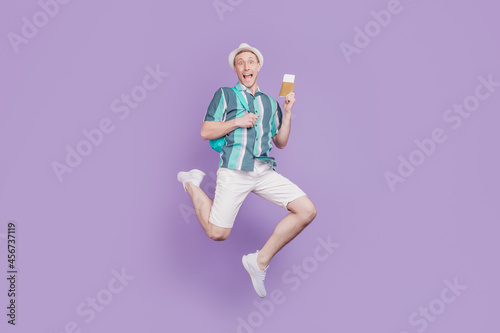 Portrait of amazed funky positive tourist guy jump run hold tickets passport on violet background
