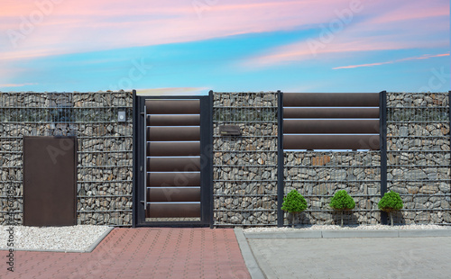 Modern wicket integrated with gabions wall. Fence made of gabions. Closed metal gate to property, part of modern stone wall fence with mailbox at street photo