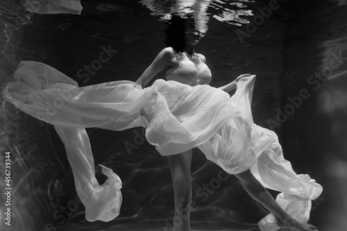 Fotografija Black and white photo where a beautiful girl in a white dress swims underwater i