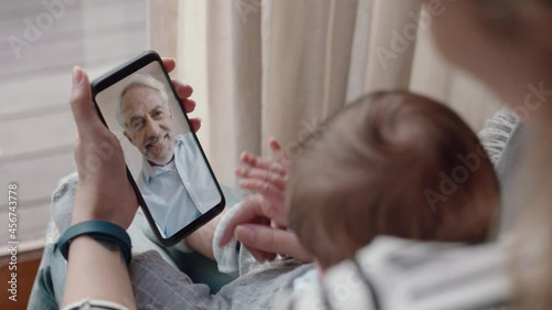 young mother and baby having video chat with grandfather using smartphone waving at newborn infant enjoying family connection photo
