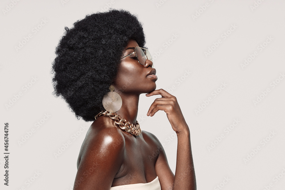 Side view of beautiful young African woman in golden jewelry keeping eyes closed and touching face - obrazy, fototapety, plakaty 