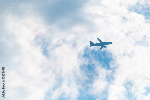 the silhouette of a passenger airliner in the blue sky behind the clouds