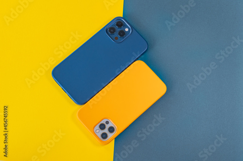 Modern mobile phones in blue and yellow leather cases on a bright background. Modern smartphones with triple lens cameras