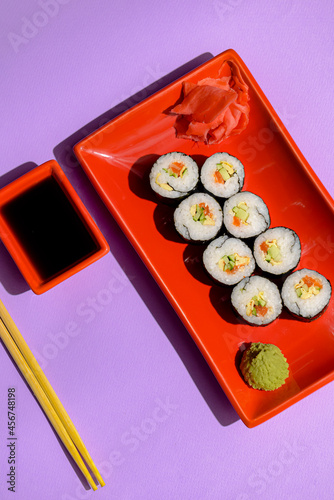 Billede på lærred Japanese sushi rolls served on a red plate with pickled ginger and wasabi sauce over colorful purple background