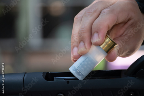 Close up of man loading a new modern shotgun shell into the magazine of his shotgun, soft and selective focus.