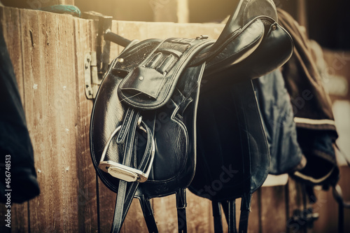Brown and black saddles hang on the stall. Horse ammunition. photo