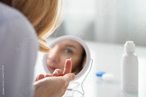 A woman sits in front of a mirror and puts contact lenses on her eyes